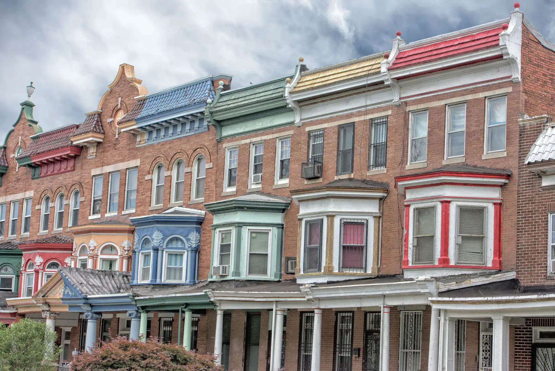 A block of colorful brick rowhomes with bay windows in a Baltimore neighborhood.